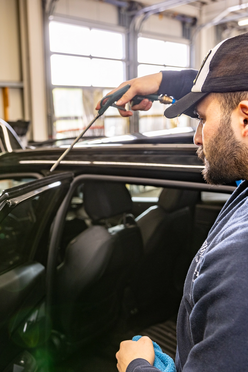 BlitzSauber das Reinigungszentrum Rellingen UG - Fahrzeugpflege - Mann mit Mütze reinigt den Innenraum eines Autos mit einem Reinigungswerkzeug und einem blauen Tuch in einer Garage