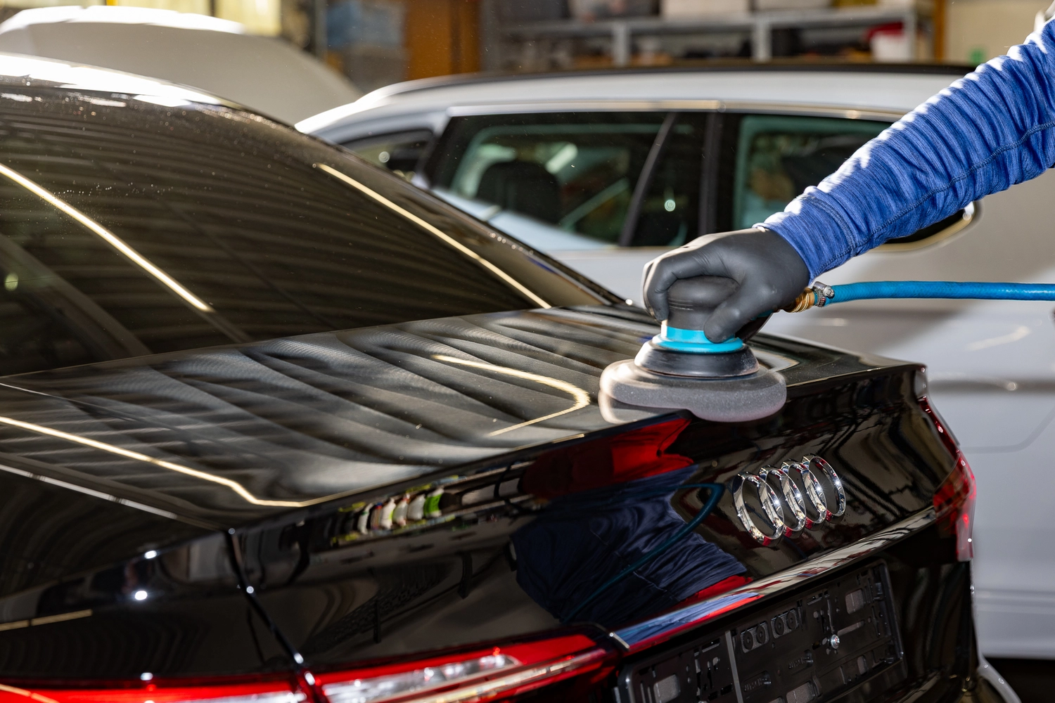 BlitzSauber das Reinigungszentrum Rellingen UG - Fahrzeugpflege - Person mit schwarzen Handschuhen poliert in einer Garage einen schwarzen Audi mit einem Elektropuffer