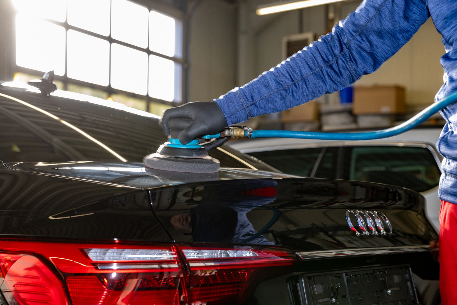 BlitzSauber das Reinigungszentrum Rellingen UG - Fahrzeugpflege - Person mit schwarzen Handschuhen poliert in einer Garage einen schwarzen Audi mit einem Elektropuffer