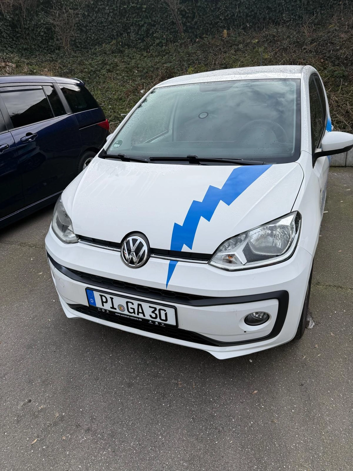 BlitzSauber das Reinigungszentrum Rellingen UG - Fahrzeugpflege - Weißer Volkswagen mit blauem Blitzaufkleber auf der Motorhaube parkt neben einem dunkelblauen Fahrzeug