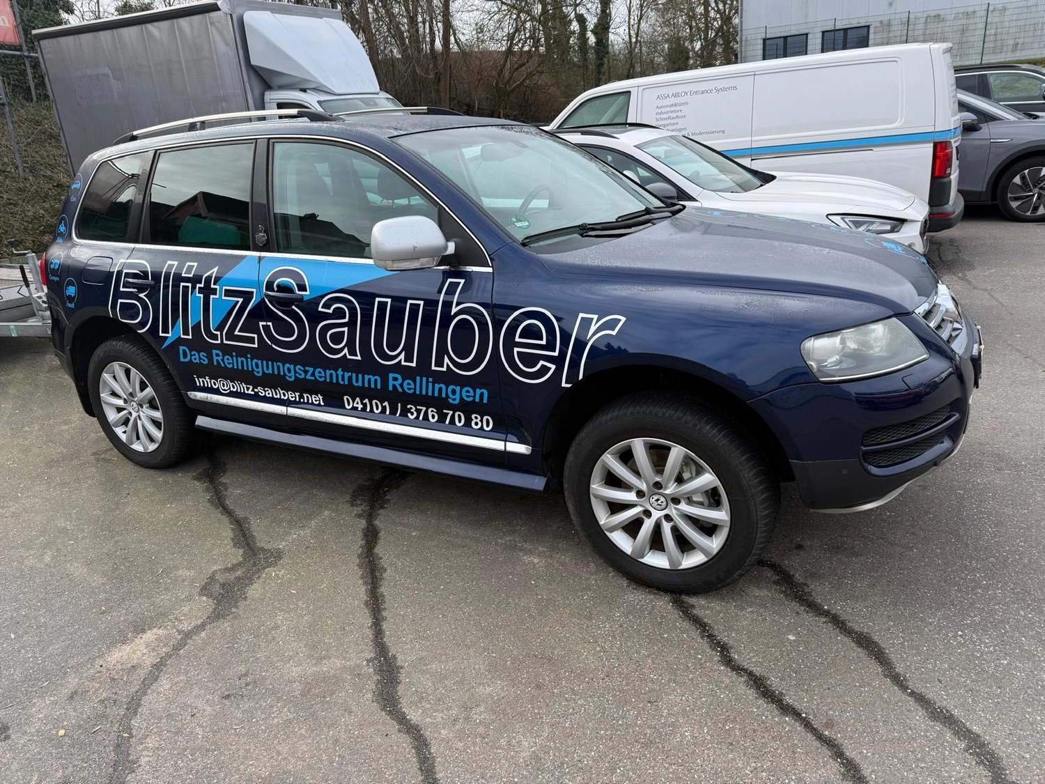 BlitzSauber das Reinigungszentrum Rellingen UG - Fahrzeugpflege - Dunkelblauer SUV mit BlitzSauber-Reinigungsdienst-Branding parkt auf Asphalt neben anderen Fahrzeugen